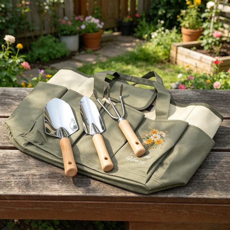 Puede incluir: Una bolsa de jard&iacute;n de lona verde con m&uacute;ltiples bolsillos, que contiene tres herramientas de jardiner&iacute;a: una paleta, una pala de mano y un cultivador de tres puntas. Las herramientas tienen mangos de madera y cabezas de metal brillante. La bolsa presenta un dise&ntilde;o floral y las palabras "Flower Glory".