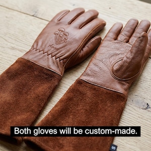 May include: A pair of brown leather gardening gloves with long suede cuffs. The gloves have a mushroom design and the name "Anna" etched on the top. The text "Both gloves will be custom-made" is at the bottom.
