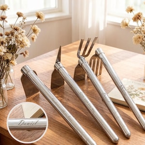 May include: Four stainless steel garden tools with personalized engravings. The tools include a hoe, a cultivator, and a garden fork. The handles are engraved with names and phrases like "Gardening with joy Anna" and "Grow with love Mia".