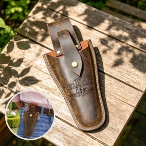 Könnte beinhalten: Braune Lederholster mit Gürtelschlaufe und Druckknopfverschluss. Das Holster hat ein florales und Werkzeugdesign mit dem eingravierten Namen "Ethan". Es ist für das Tragen am Gürtel konzipiert.
