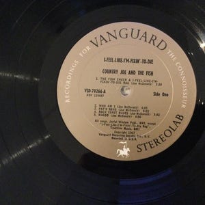 May include: A vintage vinyl record by Country Joe and the Fish, titled "I-Feel-Like-I'm-Fixin'-To-Die." The record label is tan with black text, featuring the Vanguard logo and song titles. The record is black and in good condition.