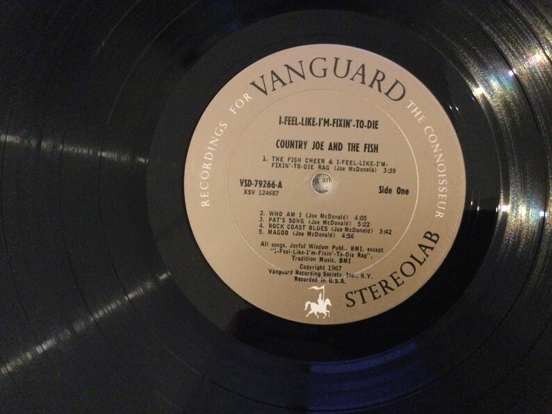 May include: A vintage vinyl record by Country Joe and the Fish, titled "I-Feel-Like-I'm-Fixin'-To-Die." The record label is tan with black text, featuring the Vanguard logo and song titles. The record is black and in good condition.