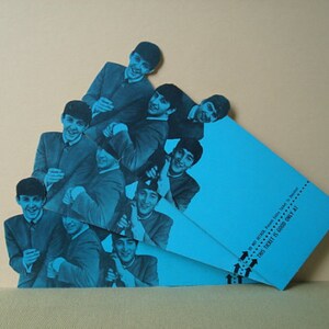 May include: A collage of images of The Beatles in blue tones, with a blue ticket in the foreground. The ticket has text that reads "THIS TICKET IS GOOD ONLY AT". The Beatles are smiling and wearing suits.