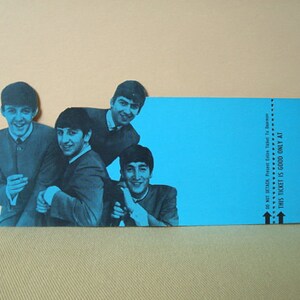 May include: A blue-toned image of The Beatles, with four band members in suits, smiling. A blue ticket-shaped element is on the right, with text that reads "THIS TICKET IS GOOD ONLY AT". The background is a light tan color.