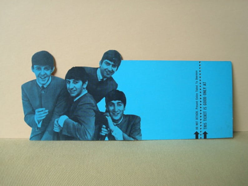 May include: A blue-toned image of The Beatles, with four band members in suits, smiling. A blue ticket-shaped element is on the right, with text that reads "THIS TICKET IS GOOD ONLY AT". The background is a light tan color.