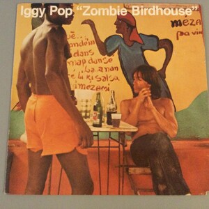 May include: Album cover for Iggy Pop's "Zombie Birdhouse" featuring a colorful illustration. The artwork depicts three figures, one in orange shorts, another in a blue and red outfit, and a third seated at a table. The background is a mix of orange, yellow, and green.