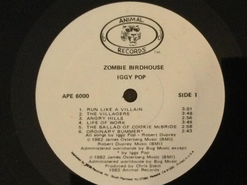 May include: A black vinyl record with a white label featuring the text "ZOMBIE BIRDHOUSE" by Iggy Pop. The label includes a logo for Animal Records and a list of songs, including "Run Like a Villain" and "Angry Hills."