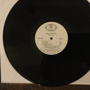 May include: A black vinyl record with a white label featuring the text "Zombie Birdhouse" and "Iggy Pop." The label also lists song titles and credits. The record is in a white paper sleeve.