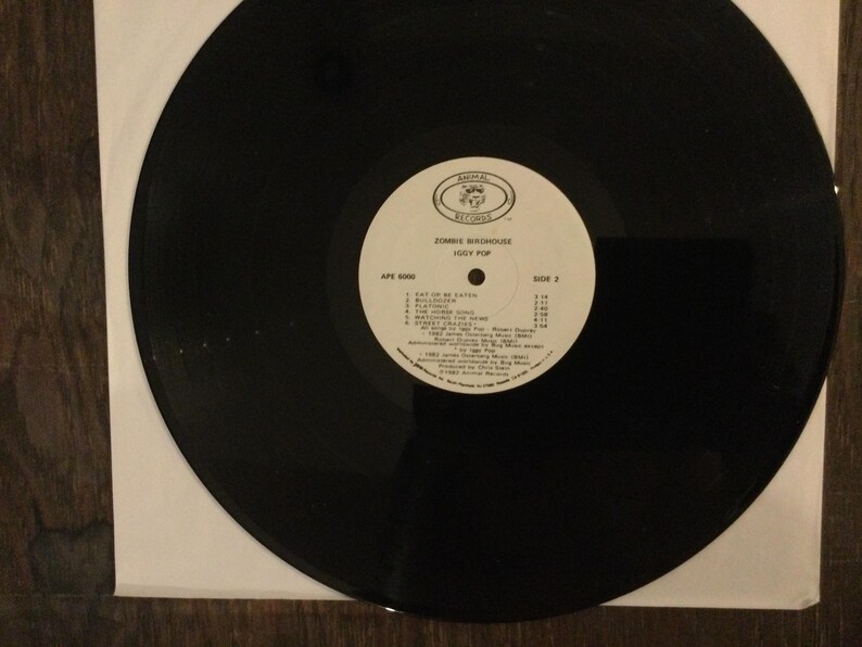 May include: A black vinyl record with a white label featuring the text "Zombie Birdhouse" and "Iggy Pop." The label also lists song titles and credits. The record is in a white paper sleeve.