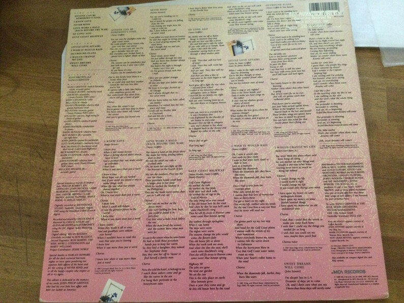 May include: The back cover of a vinyl record album with song lyrics printed in black on a pink and white background. The album's title and artist are not visible. The lyrics are arranged in columns, with a small photo in the upper left corner.