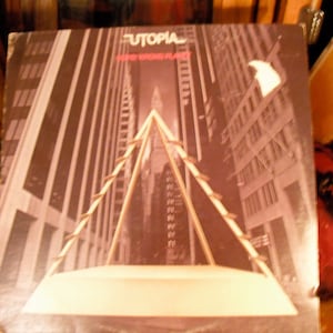 May include: Album cover for "Utopia" featuring a sepia-toned cityscape with a geometric structure in the foreground. The album title is at the top, with the words "Defe Wrong Planet" below.