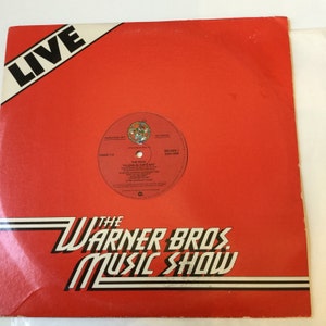 May include: A vintage vinyl record album cover for "The Who" titled "Filling in the Gaps." The cover is red with white and black text that reads "The Warner Bros. Music Show" and "LIVE." The record label is visible.