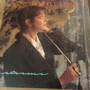 May include: Album cover featuring a woman under a floral umbrella in the rain. The album title "storms" is written in a teal script. The artist's name, "Nancy Griffith", is in pink above the image.