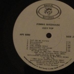 May include: A vinyl record for Iggy Pop's album "Zombie Birdhouse" on Animal Records. The label is white with black text, including song titles and timings. The record is labeled "Side 2" and has the Animal Records logo.