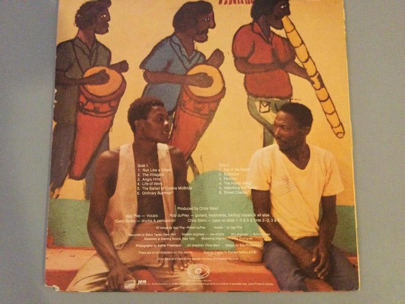 May include: Album cover featuring a colorful illustration of musicians playing drums and a wind instrument. Two men are seated in the foreground. The album title and track list are visible.