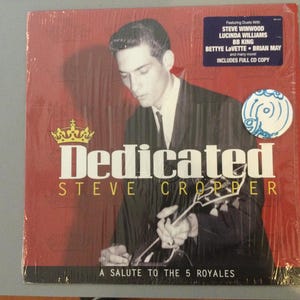 May include: A vinyl record album titled "Dedicated" by Steve Cropper. The album cover features a black and white image of a man holding a guitar against a red background. Includes a sticker with featured artists.