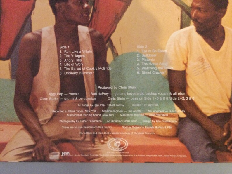 May include: Album cover featuring two men seated in front of a colorful mural. The album's tracklist is visible, including songs like "Run Like a Villain" and "Eat or Be Eaten." The album credits Iggy Pop, Clem Burke, and Chris Stein.