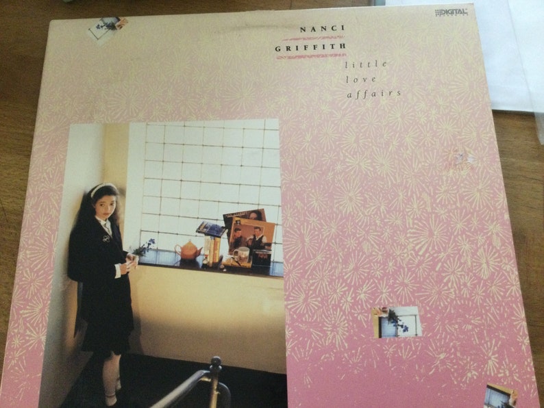 May include: Album cover for Nanci Griffith's "Little Love Affairs." The cover has a pink background with a repeating floral pattern. A photograph of a person in a black outfit is on the left. The album title and artist's name are printed in black.