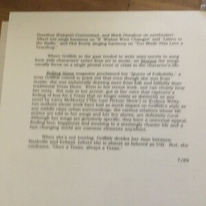 May include: A page of printed text, likely from a magazine or article, with paragraphs of text in a serif font. The text is in black ink on white paper. The page is slightly angled, and the background is a wooden surface.