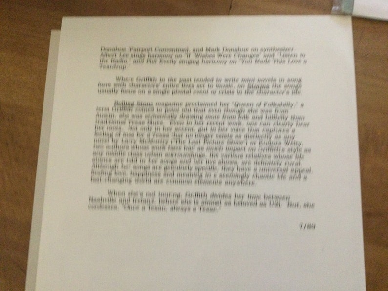 May include: A page of printed text, likely from a magazine or article, with paragraphs of text in a serif font. The text is in black ink on white paper. The page is slightly angled, and the background is a wooden surface.