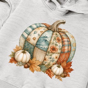 Op de afbeelding: Een lichtgrijze hoodie met een grote centrale afbeelding van een patchwork pompoen. Het pompoenontwerp bevat segmenten met blauwe oceaangolven, oranje bloemenpatronen en ruittexturen, omringd door kleine witte pompoenen en herfstbladeren.