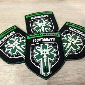 Könnte beinhalten: Vier schwarze und grüne medizinische Aufnäher mit weißen und grünen medizinischen Symbolen und Text. Die Aufnäher haben eine Schildform mit den Worten "Feldmedizin" und "Hospitaliers" in weißem Text.