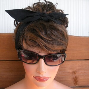 May include: A woman with brown hair is wearing a black headband and black sunglasses. The headband is tied in a bow at the top of her head.
