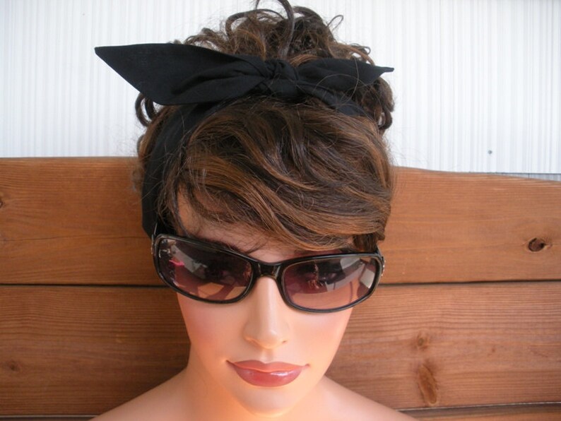 May include: A woman with brown hair is wearing a black headband and black sunglasses. The headband is tied in a bow at the top of her head.