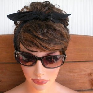 May include: A woman with brown hair wearing black sunglasses and a black headband tied in a bow.