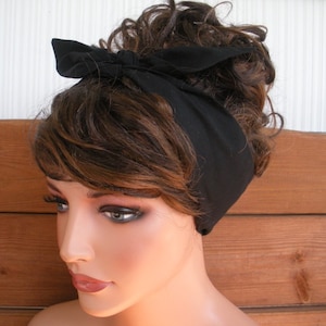 May include: A black fabric headband tied in a bow on top of a woman's head. The headband is worn over brown hair.