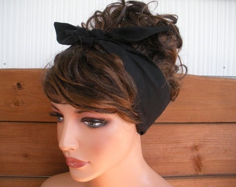 May include: A black fabric headband tied in a bow on top of a woman's head. The headband is worn over brown hair.