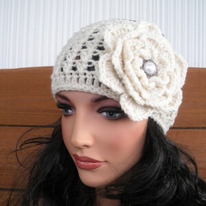 Puede incluir: Gorro de ganchillo color crema con un gran adorno floral a juego. La flor est&aacute; centrada en el lateral y presenta un bot&oacute;n decorativo. El gorro tiene un dise&ntilde;o calado.