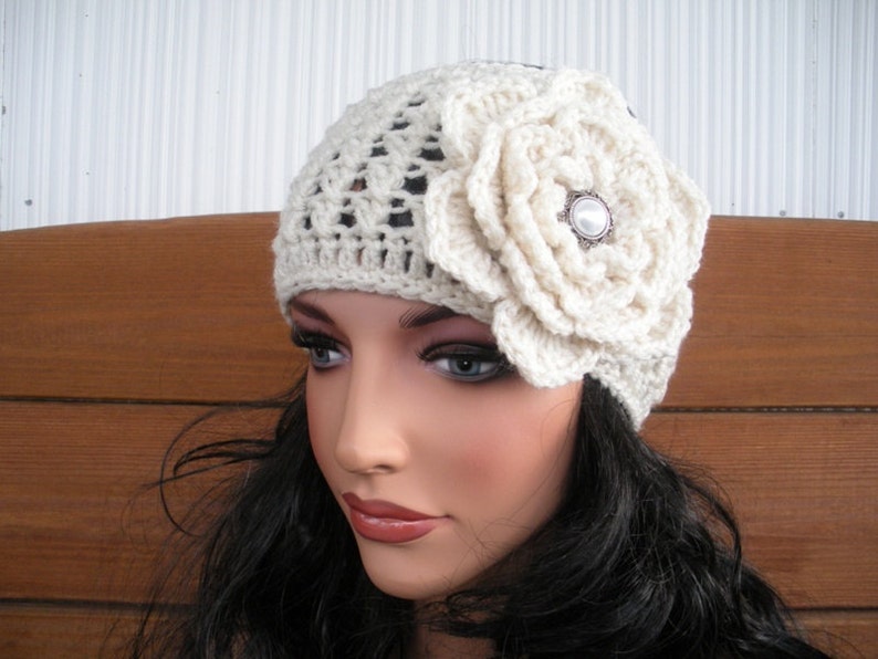 Puede incluir: Gorro de ganchillo color crema con un gran adorno floral a juego. La flor est&aacute; centrada en el lateral y presenta un bot&oacute;n decorativo. El gorro tiene un dise&ntilde;o calado.