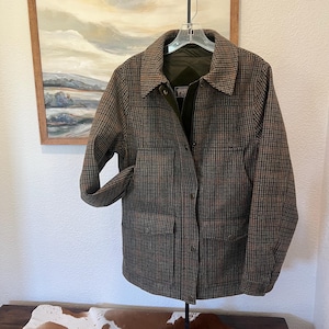 May include: A brown and black plaid jacket featuring a collared neckline, long sleeves with buttoned cuffs, and a front placket with snap closures. The jacket includes two large lower pockets with flaps and a Pendleton brand label inside.