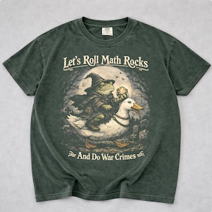 Puede incluir: Camiseta verde oscuro con el texto "Let's Roll Math Rocks And Do War Crimes". El gráfico muestra un mago rana montando un pato, sosteniendo un dado. El fondo muestra un cementerio y una luna llena.