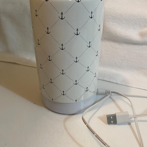 Könnte beinhalten: Ein weißer, zylindrischer Aromatherapie-Diffusor mit einem schwarzen Anker-Muster. Der Diffusor hat einen hellgrauen Sockel und ein USB-Kabel zur Stromversorgung.