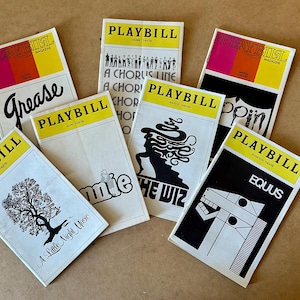 Puede incluir: Una colección de revistas Playbill vintage con títulos como "Grease" y "Equus". Cada revista tiene un encabezado amarillo con la palabra "PLAYBILL" y acentos coloridos. Las portadas muestran ilustraciones y tipografía.