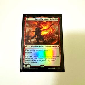 May include: A Magic: The Gathering card featuring Rograkh, Son of Rohgahh, a Kobold Warrior. The card has a fiery background with a silhouetted figure. Text includes "First strike, menace, trample, Partner" and flavor text. The card's power and toughness are 0/1.