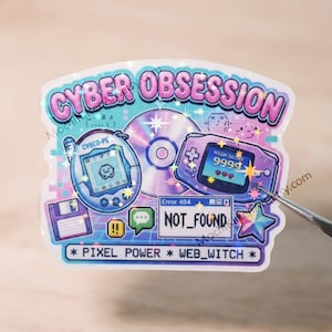以下が含まれることがあります： CYBER OBSESSIONという文字、デジタルペット機器、コンパクトディスク、携帯ゲーム機、フロッピーディスクのアイコン、Error 404 NOT_FOUNDウィンドウが描かれたホログラフィックステッカー。下部のテキストはPIXEL POWER * WEB_WITCH。
