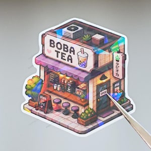 Peut inclure: Un autocollant holographique représentant une boutique de thé boba en pixel art avec une enseigne BOBA TEA et un panneau BOBA IS LIFE. La boutique possède un auvent violet, des tabourets et une porte avec un panneau OPEN et du texte japonais.