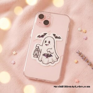 May include: A light pink smartphone case featuring a sticker of a white ghost holding a lantern and a small purple bat. The ghost is surrounded by two small black bats. The text MochiKittenArt.etsy.com is printed at the bottom of the image.