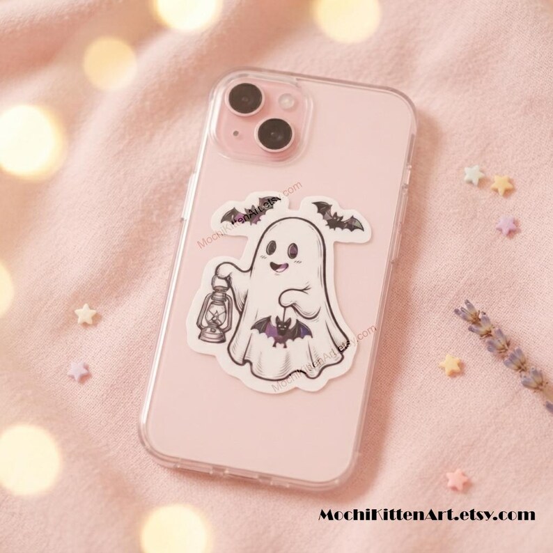 May include: A light pink smartphone case featuring a sticker of a white ghost holding a lantern and a small purple bat. The ghost is surrounded by two small black bats. The text MochiKittenArt.etsy.com is printed at the bottom of the image.