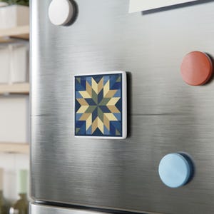 Peut inclure: Un aimant carré avec un motif d'étoile géométrique. L'étoile présente des nuances de bleu, de vert et de beige sur un fond bleu foncé. L'aimant est fixé à une porte de réfrigérateur argentée, avec d'autres aimants visibles.
