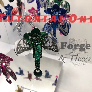 May include: A collection of colourful, metallic dragonfly ornaments hanging from a white ceiling. The dragonflies are made of chainmail and have intricate designs. The text "TUTORIAL ONLY" and "Forge & Fleece" are visible in the image.