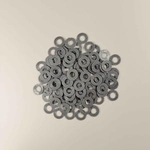 May include: A pile of small, gray, circular washers with a textured pattern. The washers are evenly distributed, with a central hole in each. The background is a solid, neutral color.