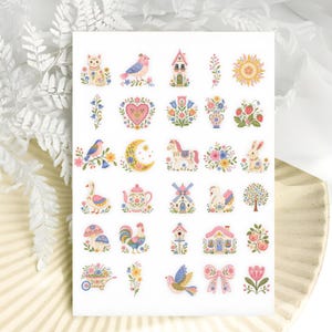 May include: A white sticker sheet featuring a grid of colorful illustrations including a cat, birds, a house, a sun, a heart, flowers, a strawberry plant, a moon, a horse, a rabbit, a goose, a teapot, a windmill, a swan, a tree, mushrooms, a rooster, a birdhouse, a cottage, fruit, a wheelbarrow, and a bow.