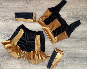 May include: A black and gold velvet costume set with a crop top, shorts, and arm warmers. The shorts have a ruffled hem.