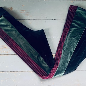 Op de afbeelding: Zwarte fluwelen broek met groene en bordeauxrode fluwelen strepen. De broek heeft een wijde pijp.
