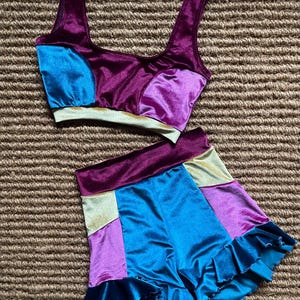 May include: A two-piece set of women's clothing in a patchwork design. The top is a crop top with wide straps, and the shorts have a ruffled hem. The colors include teal, purple, gold, and dark blue, all in a velvet-like material.
