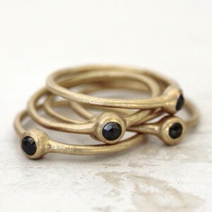 May include: Four gold rings with black gemstones. The rings are stacked on top of each other.